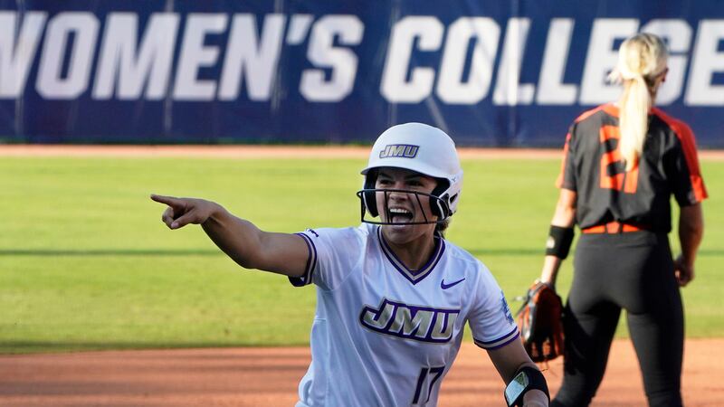 James Madison's Kate Gordon gestures to her dugout as she runs toward home plate to score...