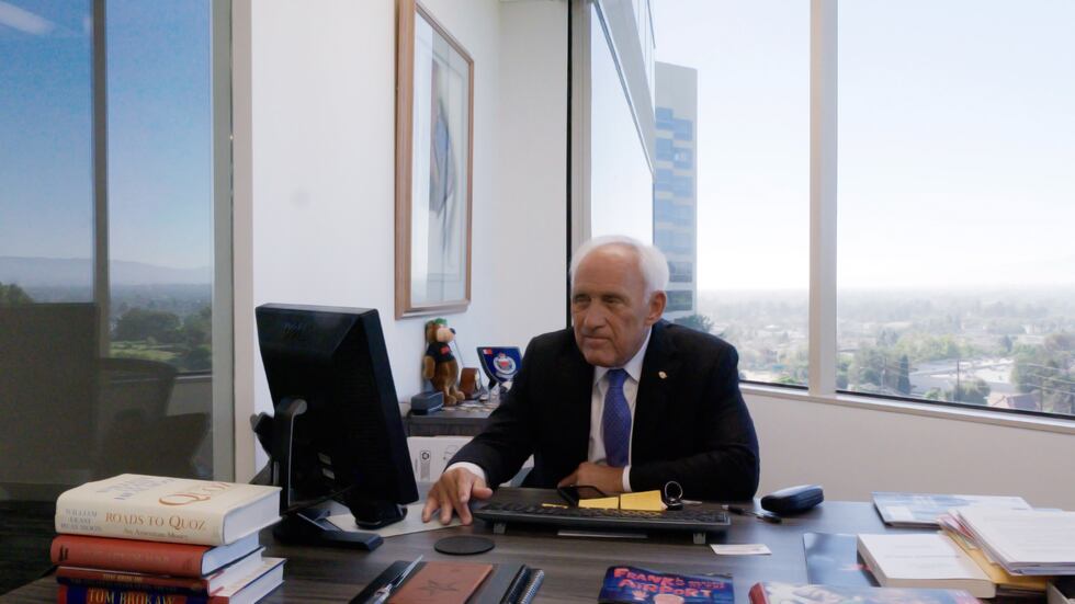 Francisco Pegueros sitting behind a desk, while looking at a computer. Behind him is a window...